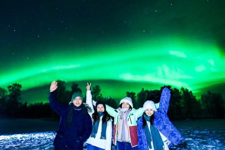 Experience the magic of the Northern Lights with friends embracing the wonder of the night sky and the beauty of Lapland's snowy landscapes during an unforgettable journey.