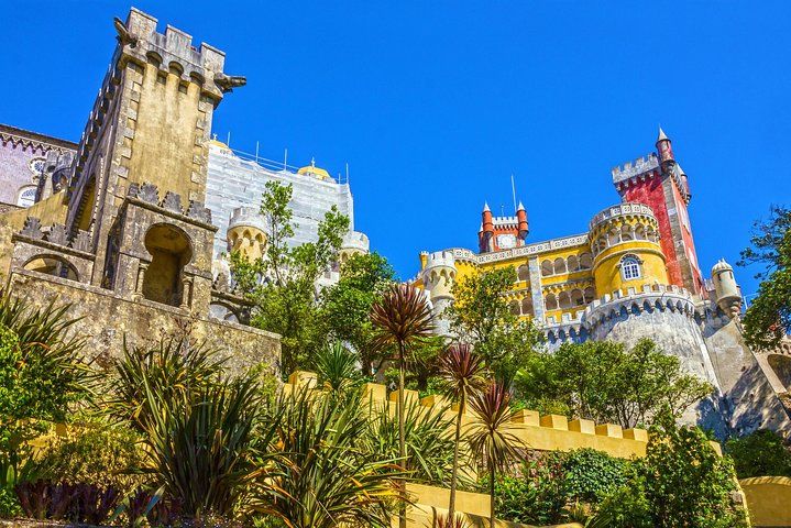 Experience the stunning architecture of Pena Palace nestled among lush gardens and a clear blue sky inviting travelers to explore the rich history and beauty of Sintra.