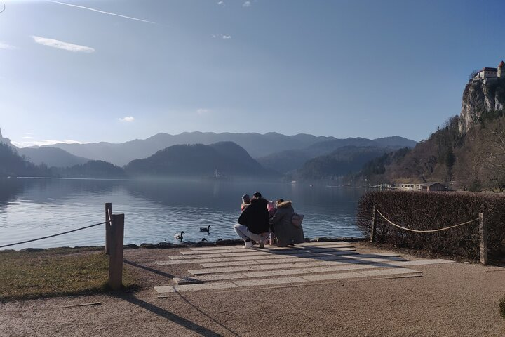 Family feeding ducks by the Bled lake. In distance is an island with a church.